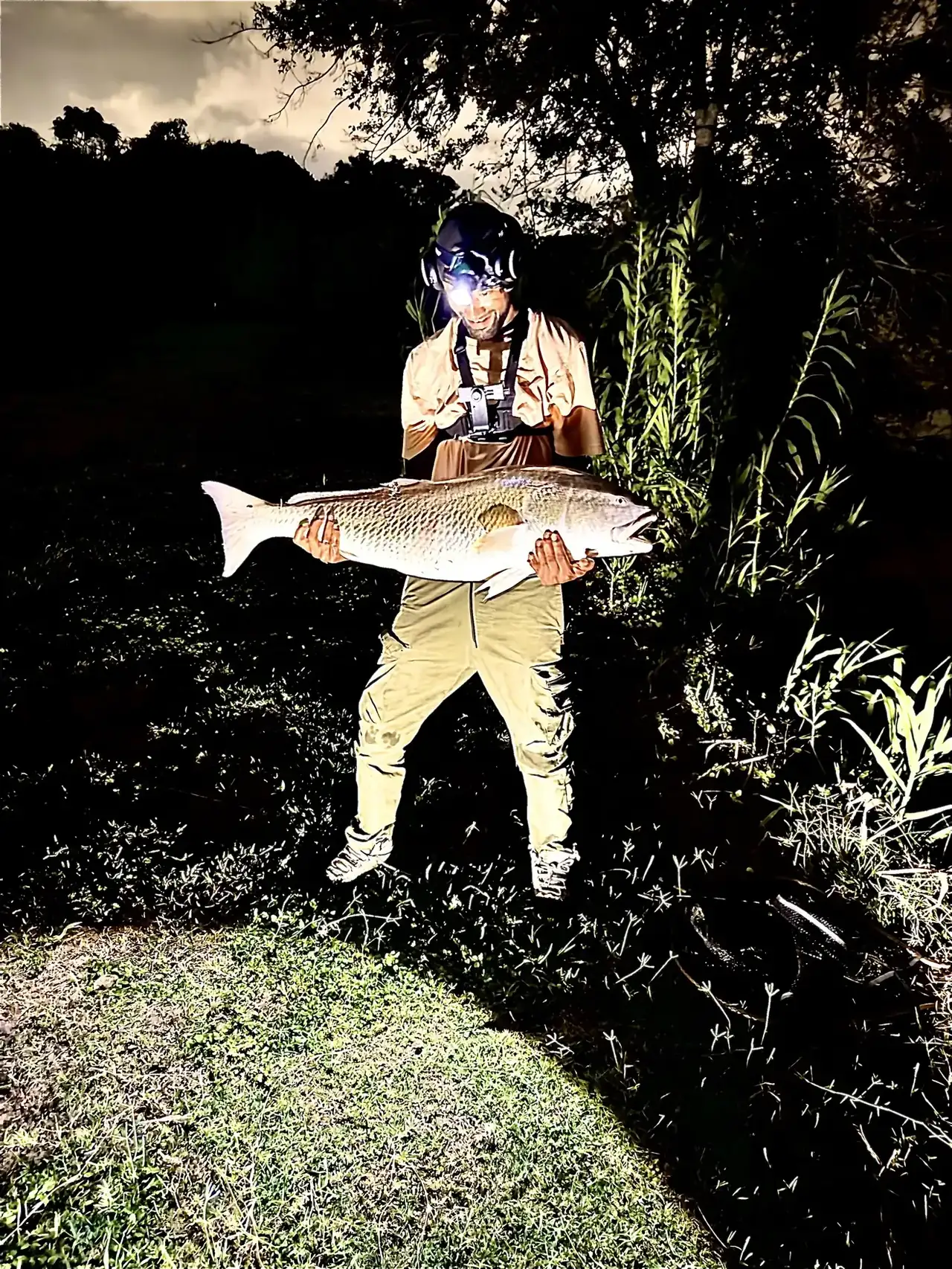 A fisherman wearing a headlamp holding a large redfish at night